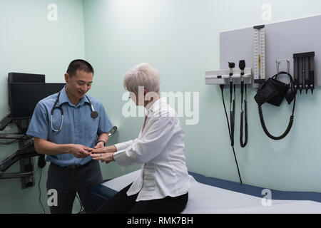 Jungen Asiatischen männlicher Arzt prüft ein älterer Patient in der Klinik Stockfoto