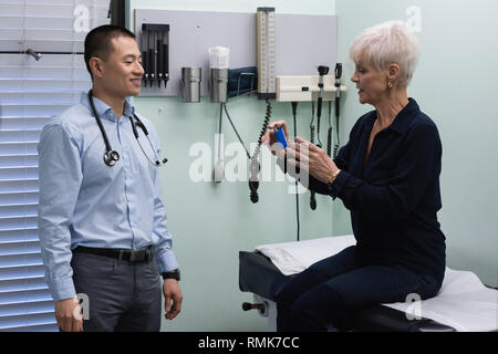 Jungen Asiatischen männlicher Arzt- und älteren Patienten diskutieren über Asthma Inhalator an der Klinik Stockfoto