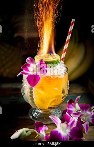 Flammender Mai Tai Cocktail in einem großen Glas mit serviert Orchideen und Limette Stockfoto