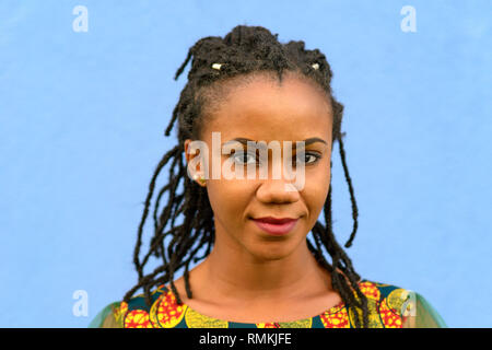 Sehr freundliche junge afrikanische amerikanische Frau mit geflochtenem dreadlock Frisur im Kopf und Schultern Portrait auf Blau Stockfoto