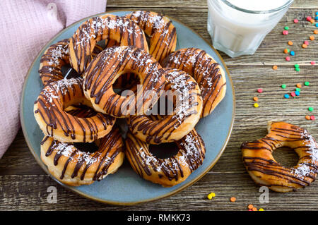 Hausgemachte klassische Donuts mit Schokolade und Kokos Flocken auf einer hölzernen Hintergrund. Stockfoto