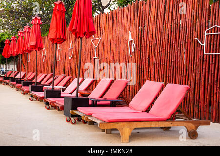 Rot Sonnenschirm und Liegestühle bei Sonnenaufgang am Außenpool. Stockfoto