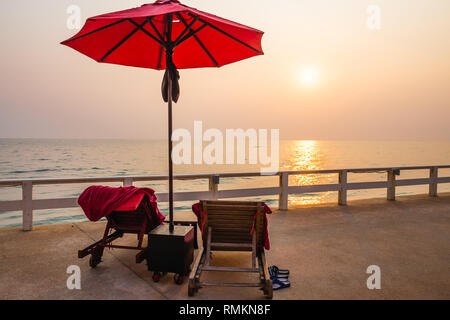 Rot Sonnenschirm und Liegestühle bei Sonnenaufgang am Außenpool. Stockfoto