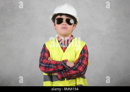 Kleines Kind Bauarbeiter in weißen Helm und Sonnenbrille vor grauem Hintergrund Stockfoto