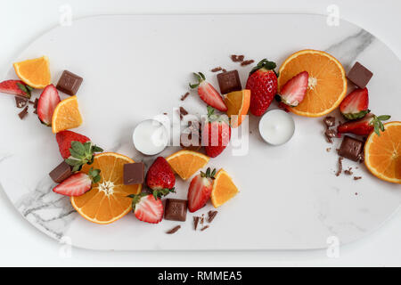 Flach Zusammensetzung eines Mix aus Erdbeeren, orange, Schokolade und Kerzen auf einem hellen Marmorboden Hintergrund Stockfoto