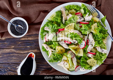 Ansicht von oben von Huhn, frischem Salat, Ananas, Radieschen und Gurken Salat auf einem weißen Teller auf einen Holztisch mit Balsamico Dressing und Bro Stockfoto