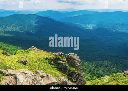 Felsige Klippe auf einem grasigen Hang über dem Tal. schönen Sommer Landschaft in den Bergen. Riesige ridge in der Ferne. Ansicht von oben Stockfoto