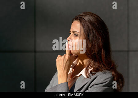Nachdenkliche Frau, die mit einem Problem mit Ihrem Finger auf ihre Lippen in einem Profil anzeigen im freien Raum mit kopieren Stockfoto