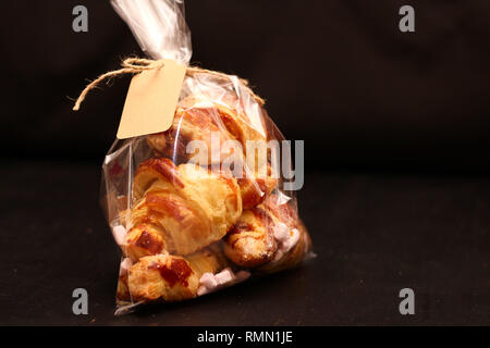 Frische hausgemachte Französische Croissants mit Füllung in einem transparenten Zellophan Beutel mit einem Tag auf einem Schwarzen Tisch Stockfoto