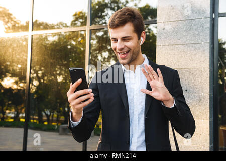 Portrait von Happy Geschäftsmann in Anzug holding Handy im Freien stehend gegen Gebäude Stockfoto