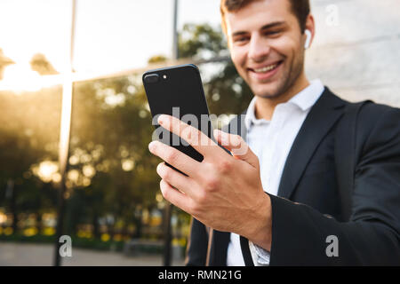 Foto von büroangestellter in der Klage holding Handy im Freien stehend gegen Gebäude Stockfoto