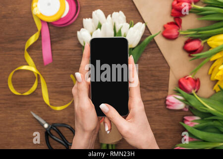 7/8-Ansicht von Floristen unter Foto von Tulip Blumenstrauß auf dem Smartphone Stockfoto