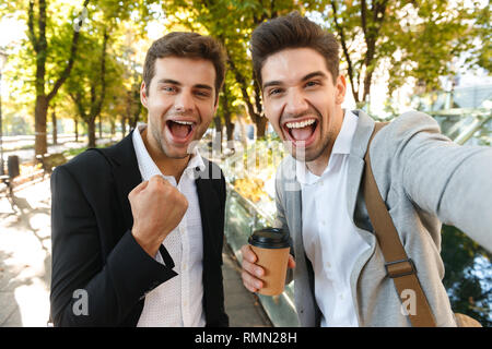 Bild von fröhlichen Geschäftsleute in Anzügen, die selfie Foto auf Handy outdoor Wandern durch grüne Park mit Kaffee zum Mitnehmen Stockfoto