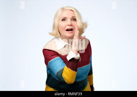 Senior hübsche Frau die Hand in der Nähe von Mund und sagt Geheimnis. Stockfoto