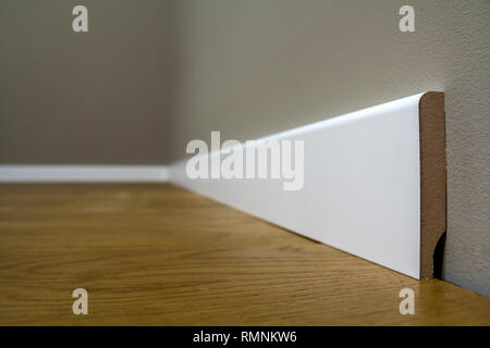 Holz- oder Kunststoff Weiß, Sockel Installation in großen leeren Raum auf Holzboden und weiß verputzt verputzten Wänden Hintergrund. Details im Innenraum. Stockfoto