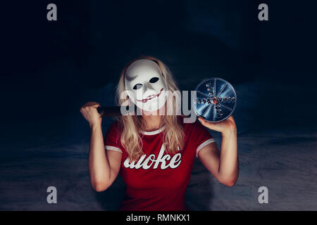 Blonde Frau unter weißen Maske mit gruseligen blutigen Lächeln, halten Sie Messer und Blade in Selbstverteidigung, Horror-Konzept, das Tragen der roten T-Shirt mit weißen Buchstaben Stockfoto