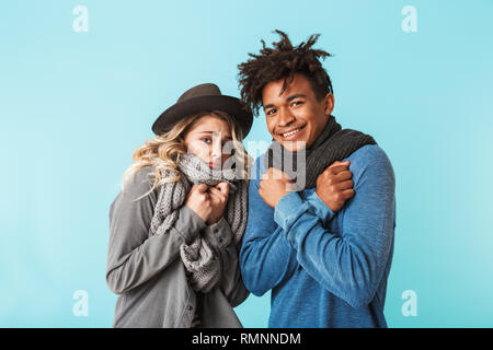 Lächelnden jungen gemischtrassiges Paar tragen Schals stehen über blauen Hintergrund isoliert, schütteln Stockfoto