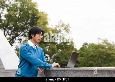 Lächelnd Asian Business Mann mit Laptop im Freien Stockfoto