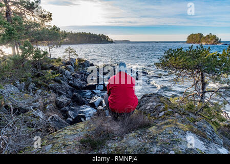 Mann im roten Mantel mit Blick auf den See Vattern in Motala in Schweden Stockfoto