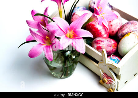 Rosa Lilie Blumen und Ostern Eier in einem Korb auf Weiß Stockfoto