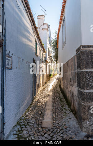 Verwinkelten engen, kopfsteingepflasterten Gasse entfernt zwischen traditionellen, weiß getünchten Häuser aus Stein in Cascais Portugal führenden Stockfoto