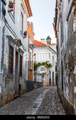 Verwinkelten engen, kopfsteingepflasterten Gasse entfernt zwischen traditionellen verfallen und renoviert, weiß getünchten Häuser aus Stein in Cascais Portugal führenden Stockfoto