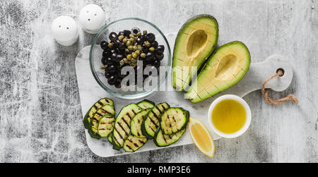 Banner von Zutaten für Frühjahr Salat von reife Avocado, gegrillte Zucchini, schwarze Oliven, Kapern und Zitrone Dressings, gesunden veganen Küche für die whol Stockfoto