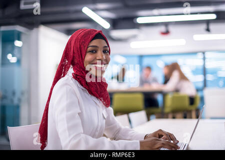 Junge moderne Black Muslim business Frau mit einem roten Kopftuch, Arbeiten am Laptop im Startup Office. Vielfalt, multirassischen Konzept Stockfoto
