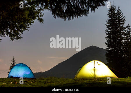 Zwei hell leuchtende, touristische Zelte auf der grünen Wiese Wald Lichtung auf dunklen Berg und dem klaren, blauen Sternenhimmel Kopie Raum Hintergrund. Tourismus, Nacht campin Stockfoto