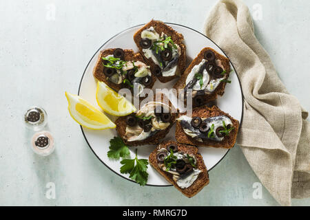 Sandwiches mit Sardinen, mariniert in Olivenöl mit Knoblauch und Roggenbrot. Sommer leichte italienische Vorspeise mit Zitrone und Petersilie Stockfoto