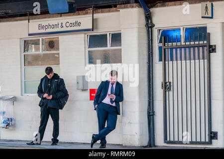 Zwei Passagiere auf der Suche auf ihre Handys auf der Plattform in der Elephant & Castle-Station im Süden Londons, beim Warten auf einen Zug. Stockfoto