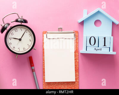 1 April Fool's Day Holz- Kalender, Notizbuch, Uhr, Stift. Flach auf einem rosa Hintergrund. Stockfoto