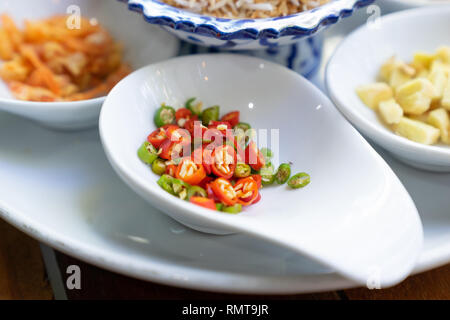 Die in Scheiben geschnittenen roten und grünen Chili auf Weiß Löffel für miang kum Zutat schließen Stockfoto