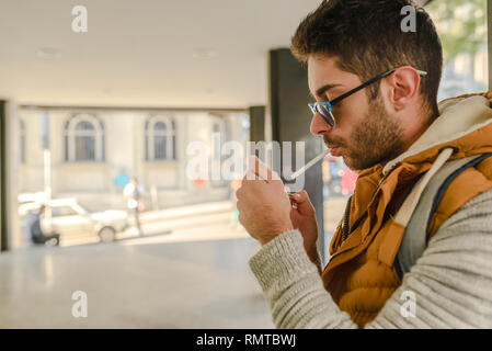 Junge schöne Hipster mit orange Jacke Sonnenbrille und genießen eine Zigarette auf der Straße. Stockfoto