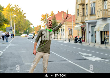 Junger Mann mit grünen Kopfhörer stoppen Taxi in der Stadt. Stockfoto