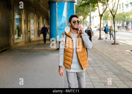 Junge Hipster mit orange Jacke und Sonnenbrille mit seinem Smart Phone in der Stadt. Stockfoto