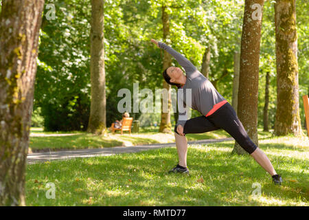 Kompromisslos sportliche reife Frau Yoga Übungen in einem Park einen Arm in einem vollen Ausdehnung in ein Gesundheits- und Fitness Concept Stockfoto