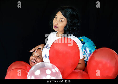 Paar in Blue Jeans mit roten Luftballons ihren Geburtstag feiern gemeinsam spielerisch Stockfoto