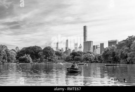 Paare, die in einem Ruderboot auf dem See im Central Park mit dem Mid Town Manhattan Skyline unter wispy Wolken am Horizont, Schwarz und Weiß. Stockfoto