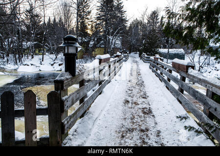 Fußgängerbrücke mit Laternen und schneebedeckten Pflanzmaschine Boxen, Kreuzung ein teilweise gefrorenen schnell fließenden Fluss Stockfoto