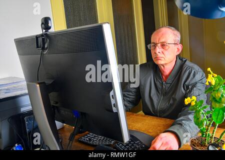 Im mittleren Alter Mann mit Brille am Schreibtisch sitzen. Reifer Mann mit Personal Computer. Senior Concept Stockfoto