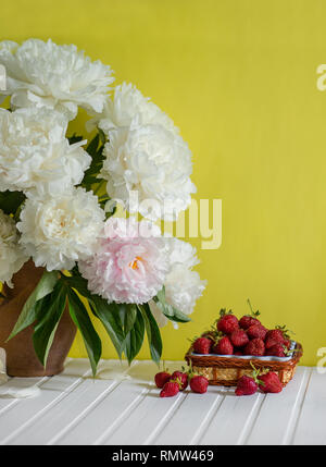 Einen großen Blumenstrauß von Pfingstrosen in Vase aus Ton und eine Schüssel Erdbeeren auf einem Baum. Romantische Stimmung. Stockfoto