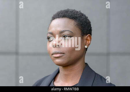 Close-up halbe Umdrehung Portrait von Kurzhaarige schwarze Frau in business Blazer und mit kleinen Ohrringe, weg schauen mit ruhigen Gesicht. Ständigen freien Aga Stockfoto