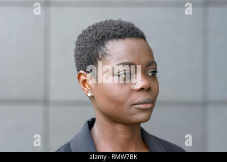 Close-up halbe Umdrehung Portrait von Kurzhaarige schwarze Frau in business Blazer und mit kleinen Ohrringe, weg schauen mit ruhigen Gesicht. Ständigen freien Aga Stockfoto