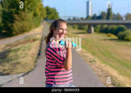 Gerne passen junge Frau voller Vitalität, die in frühen Morgen Licht arbeiten in einem städtischen Park lächelte, als sie hebt Hantel Gewichte in einer gesunden, aktiven l Stockfoto