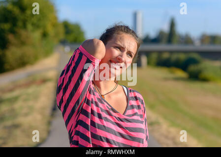 Junge Frau Joggen leidet eine Muskelverletzung stehend hält Hals und unteren zurück, während verzog das Gesicht vor Schmerzen auf der Landstraße, Oberkörper hautnah Stockfoto