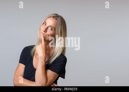 Spekulative Frau in die Kamera schaut mit großen Augen nachdenklichen Ausdruck mit den Kopf zur Seite geneigt und der Hand ihr Kinn über Grau mit kopieren Stockfoto