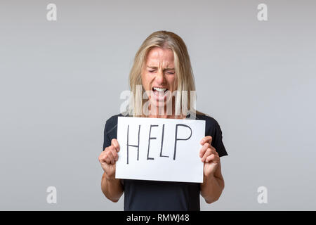 Verzweifelt reife Frau holding Blatt Papier mit Hilfe Schriftzug auf weißem Hintergrund Stockfoto