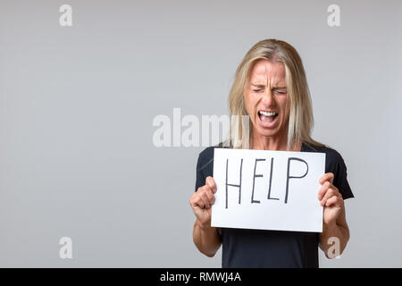 Verzweifelt reife Frau holding Blatt Papier mit Hilfe Schriftzug auf weißem Hintergrund Stockfoto