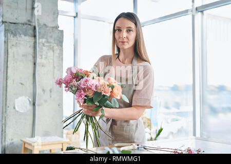 Junge Frau mit Haufen frischen rosa Blumen und Rosen, Blumenstrauß, während in Ihrem Studio arbeiten Stockfoto